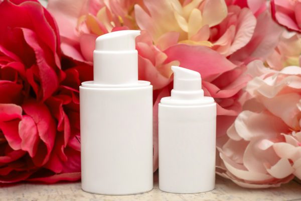 Cosmetic set of two plastic containers of bottles with dispenser on background of pink peony flowers. Stylish layout. Organic skin care concept. Mock up