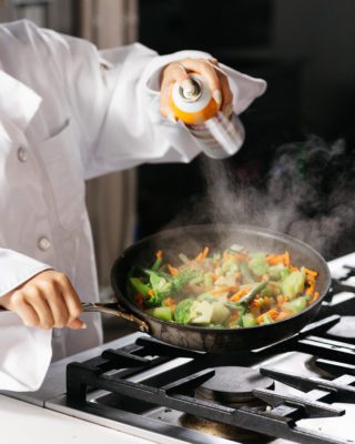 A chef using cooking spray on a pan