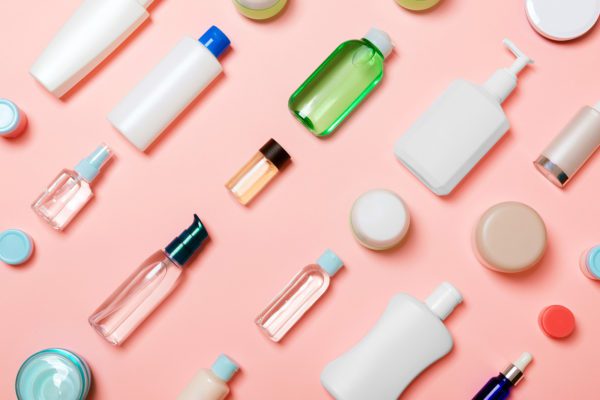 Top view of different cosmetic bottles and container for cosmetics on pink background. Flat lay composition with copy space.