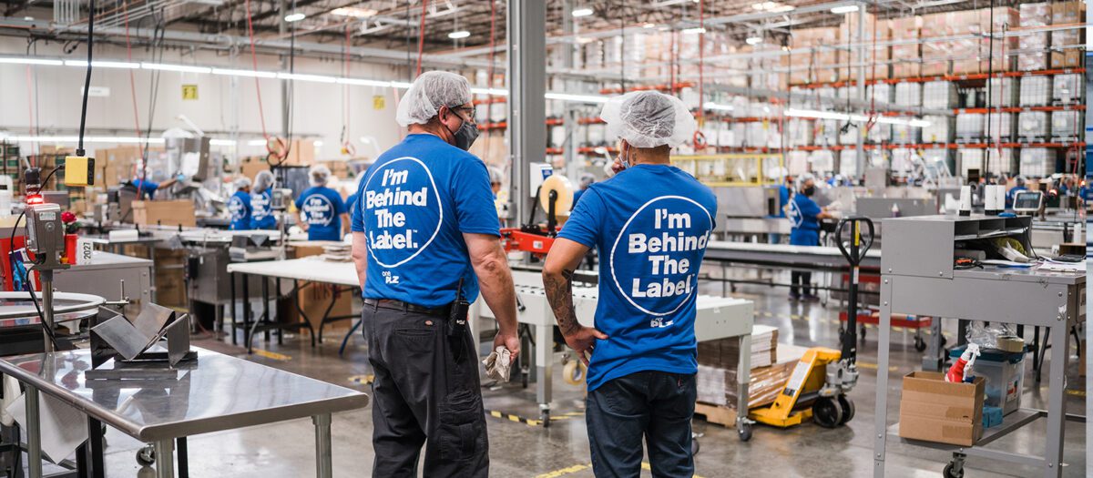 back view of two PLZ employees in behind the label T-Shirts