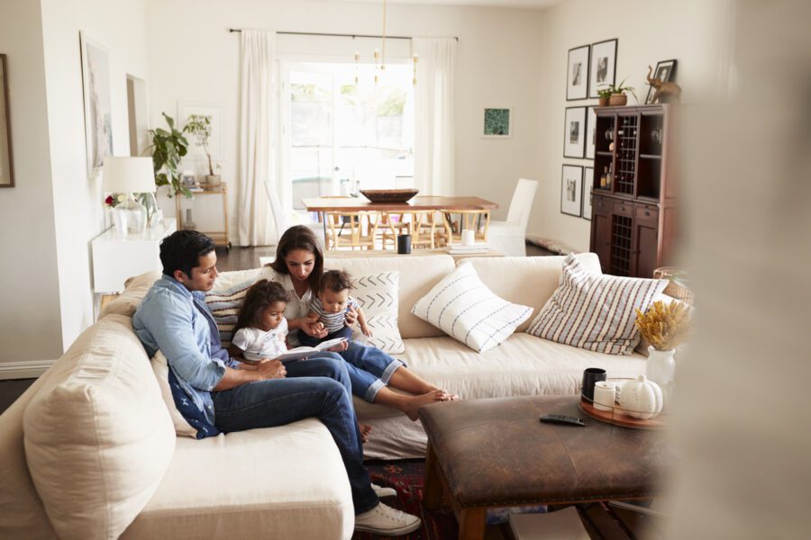 young-hispanic-family-sitting-on-sofa-reading-a-book-together-in-the-living-room-seen-from-doorway