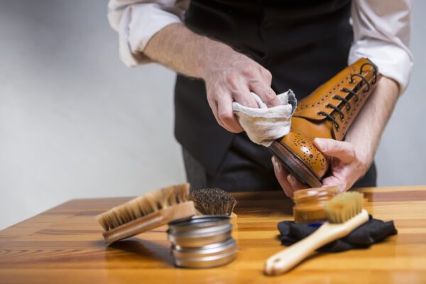 Closeup of Hands of Man Cleaning Premium Derby Boots With Variety of Brushes and Accessories