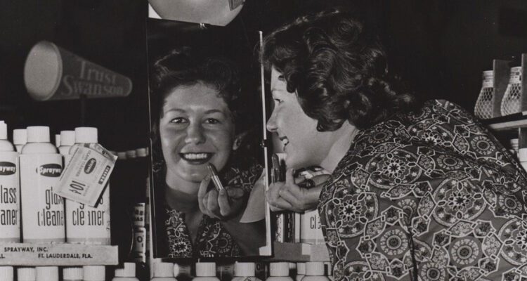 woman applying lipstick in front of mirror