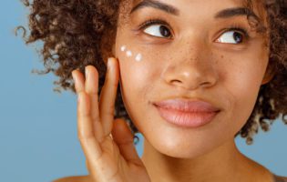 young black women putting lotion or cream on her face with blue background