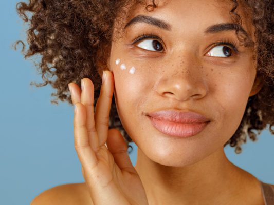 young black women putting lotion or cream on her face with blue background