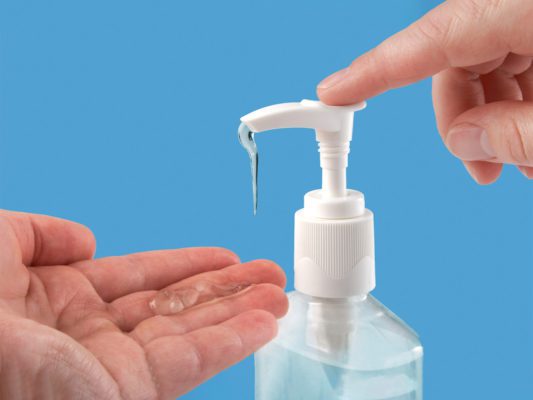 Hand pumping liquid hand sanitizer into other hand on blue background
