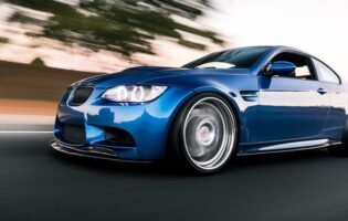 Blue BMW M3 driving on the road with a clear sky overhead