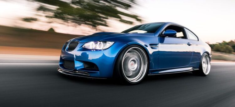 Blue BMW M3 driving on the road with a clear sky overhead